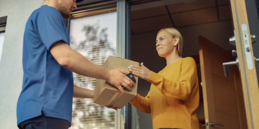 Młoda kobieta odbierająca paczkę kurierską przy drzwiach